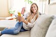 © Krakenimages.com - Young blonde woman using smartphone sitting on the sofa at home.