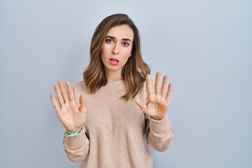Young woman standing over isolated background moving away hands palms showing refusal and denial with afraid and disgusting expression. stop and forbidden.