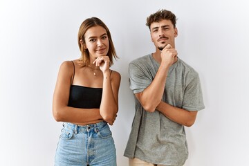 Sticker - Young beautiful couple standing together over isolated background looking confident at the camera smiling with crossed arms and hand raised on chin. thinking positive.