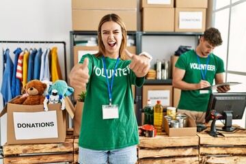 Canvas Print - Young blonde girl wearing volunteer t shirt at donation stand approving doing positive gesture with hand, thumbs up smiling and happy for success. winner gesture.