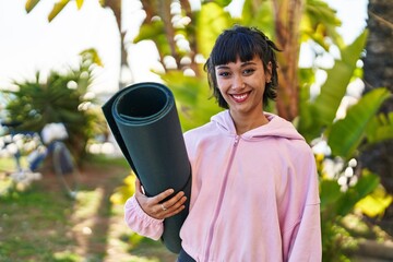 Wall Mural - Young woman holding yoga mat standing at park