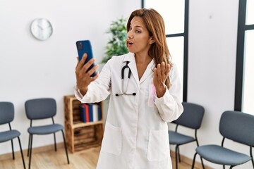 Canvas Print - Young latin woman wearing doctor uniform having video call at clinic waiting room