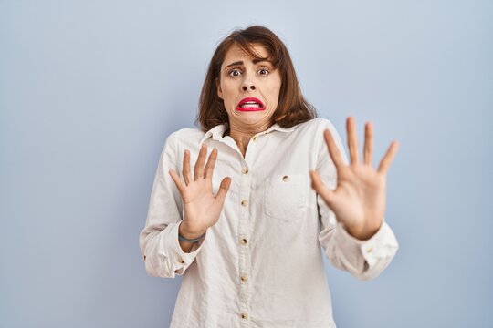 young beautiful woman standing casual over blue background afraid and terrified with fear expression