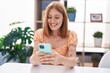 © Krakenimages.com - Young redhead woman using smartphone sitting on table at home
