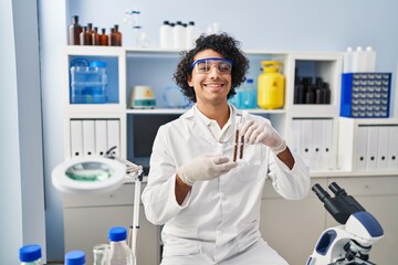 Poster - Young hispanic man wearing scientist uniform holding test tubes at laboratory