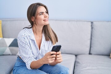 Wall Mural - Young woman using smartphone sitting on sofa at home