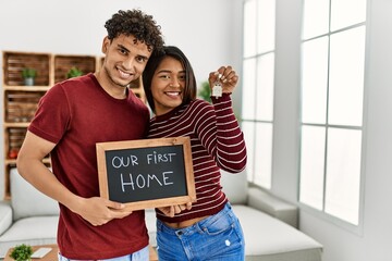 Poster - Young latin couple smiling happy holding our first home blackboard and key at house.