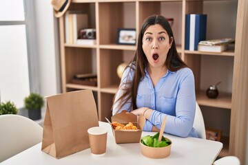 Poster - Young brunette woman eating take away food at home scared and amazed with open mouth for surprise, disbelief face