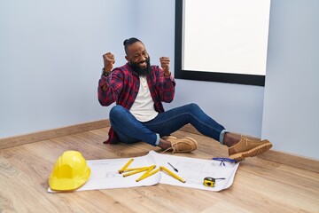 Poster - African american man sitting on the floor at new home looking at blueprints very happy and excited doing winner gesture with arms raised, smiling and screaming for success. celebration concept.