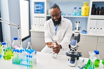 Sticker - Young african american man wearing scientist uniform using sanitizer gel hands at laboratory