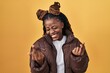 African woman with braided hair standing over yellow background showing middle finger doing fuck you bad expression, provocation and rude attitude. screaming excited
