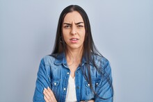 Hispanic Woman Standing Over Blue Background Skeptic And Nervous, Disapproving Expression On Face With Crossed Arms. Negative Person.