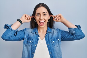 Canvas Print - Hispanic woman standing over blue background smiling pulling ears with fingers, funny gesture. audition problem