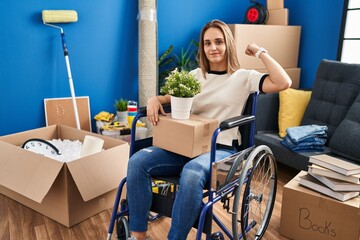 Canvas Print - Young woman sitting on wheelchair moving to a new home strong person showing arm muscle, confident and proud of power