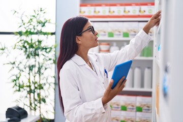 Wall Mural - Young beautiful hispanic woman pharmacist using touchpad working at pharmacy