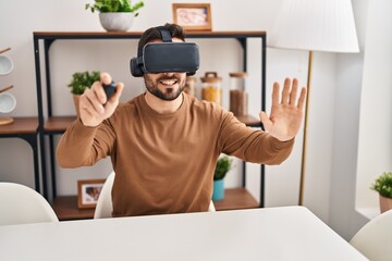 Wall Mural - Young hispanic man playing video game using virtual reality glasses at home