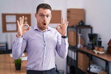 Poster - Young hispanic man at the office looking surprised and shocked doing ok approval symbol with fingers. crazy expression