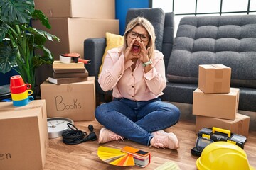 Poster - Young hispanic woman moving to a new home sitting on the floor shouting angry out loud with hands over mouth