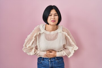 Poster - Young asian woman standing over pink background with hand on stomach because indigestion, painful illness feeling unwell. ache concept.