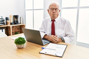 Canvas Print - Senior man working at the office using computer laptop making fish face with lips, crazy and comical gesture. funny expression.