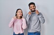 © Krakenimages.com - Young hispanic couple standing together smiling with open mouth, fingers pointing and forcing cheerful smile
