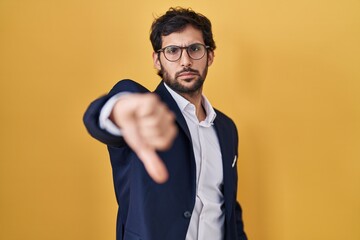 Poster - Handsome latin man standing over yellow background looking unhappy and angry showing rejection and negative with thumbs down gesture. bad expression.