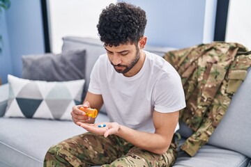 Wall Mural - Young arab man army soldier taking pills sitting on sofa at home