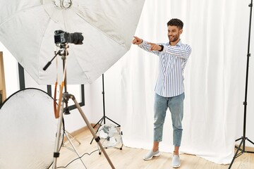 Wall Mural - Arab young man posing as model at photography studio pointing to you and the camera with fingers, smiling positive and cheerful