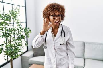 Canvas Print - Young african american woman wearing doctor uniform and stethoscope smiling with hand over ear listening an hearing to rumor or gossip. deafness concept.