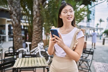 Wall Mural - Young chinese girl smiling happy using smartphone at the city.