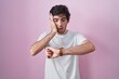 © Krakenimages.com - Young hispanic man standing over pink background looking at the watch time worried, afraid of getting late