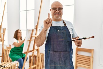 Sticker - Middle age hispanic man at art studio surprised with an idea or question pointing finger with happy face, number one