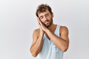 Sticker - Young handsome man standing over isolated background sleeping tired dreaming and posing with hands together while smiling with closed eyes.