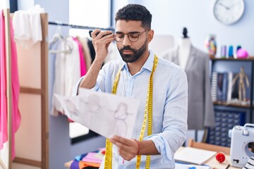 Poster - Young arab man tailor talking on smartphone looking clothing design at tailor shop