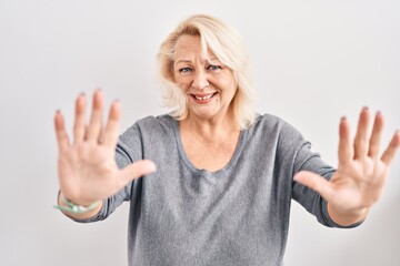 Middle age caucasian woman standing over white background doing stop gesture with hands palms, angry and frustration expression