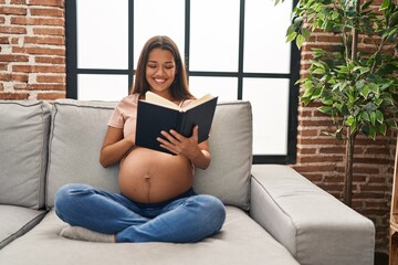 Canvas Print - Young latin woman pregnant touching belly reading book at home