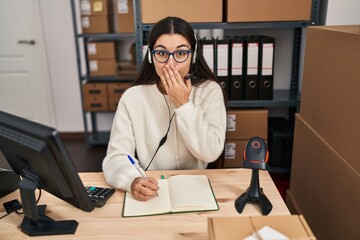 Poster - Young hispanic woman working at small business ecommerce wearing headset covering mouth with hand, shocked and afraid for mistake. surprised expression