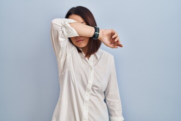 Sticker - Young hispanic woman standing over white background covering eyes with arm, looking serious and sad. sightless, hiding and rejection concept