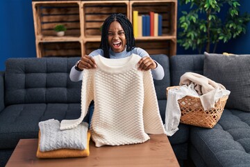 Wall Mural - African american woman folding clean laundry celebrating crazy and amazed for success with open eyes screaming excited.