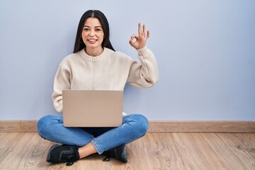 Sticker - Young woman using laptop sitting on the floor at home smiling positive doing ok sign with hand and fingers. successful expression.