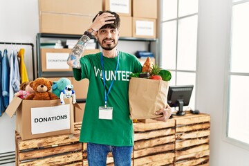 Sticker - Hispanic man with beard wearing volunteer t shirt at donations point stressed and frustrated with hand on head, surprised and angry face