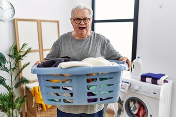 Canvas Print - Senior caucasian man holding detergent bottle at laundry room smiling and laughing hard out loud because funny crazy joke.