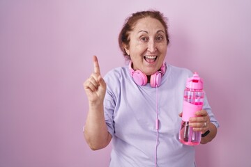 Sticker - Senior woman wearing sportswear and headphones smiling amazed and surprised and pointing up with fingers and raised arms.