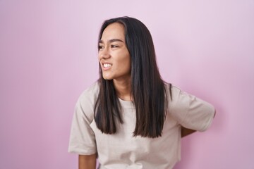 Poster - Young hispanic woman standing over pink background suffering of backache, touching back with hand, muscular pain