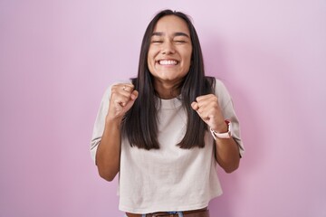 Canvas Print - Young hispanic woman standing over pink background excited for success with arms raised and eyes closed celebrating victory smiling. winner concept.