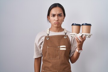Wall Mural - Young hispanic woman wearing professional waitress apron holding coffee skeptic and nervous, frowning upset because of problem. negative person.