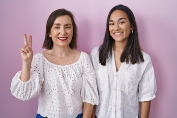 Wall Mural - Hispanic mother and daughter together showing and pointing up with fingers number two while smiling confident and happy.