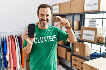 Sticker - Middle age man with beard wearing volunteer t shirt holding smartphone smiling and confident gesturing with hand doing small size sign with fingers looking and the camera. measure concept.