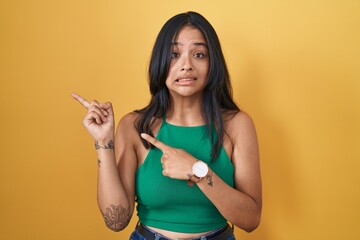 Sticker - Brunette woman standing over yellow background pointing aside worried and nervous with both hands, concerned and surprised expression