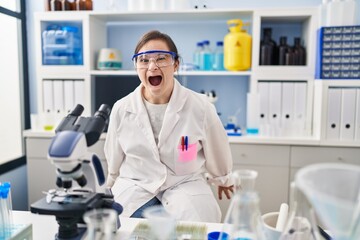 Sticker - Hispanic girl with down syndrome working at scientist laboratory angry and mad screaming frustrated and furious, shouting with anger. rage and aggressive concept.